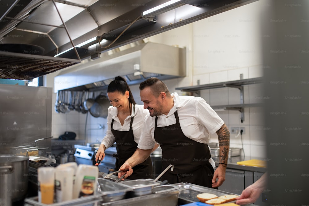 Uno chef e un cuoco felici che lavorano sui loro piatti all'interno nella cucina del ristorante.