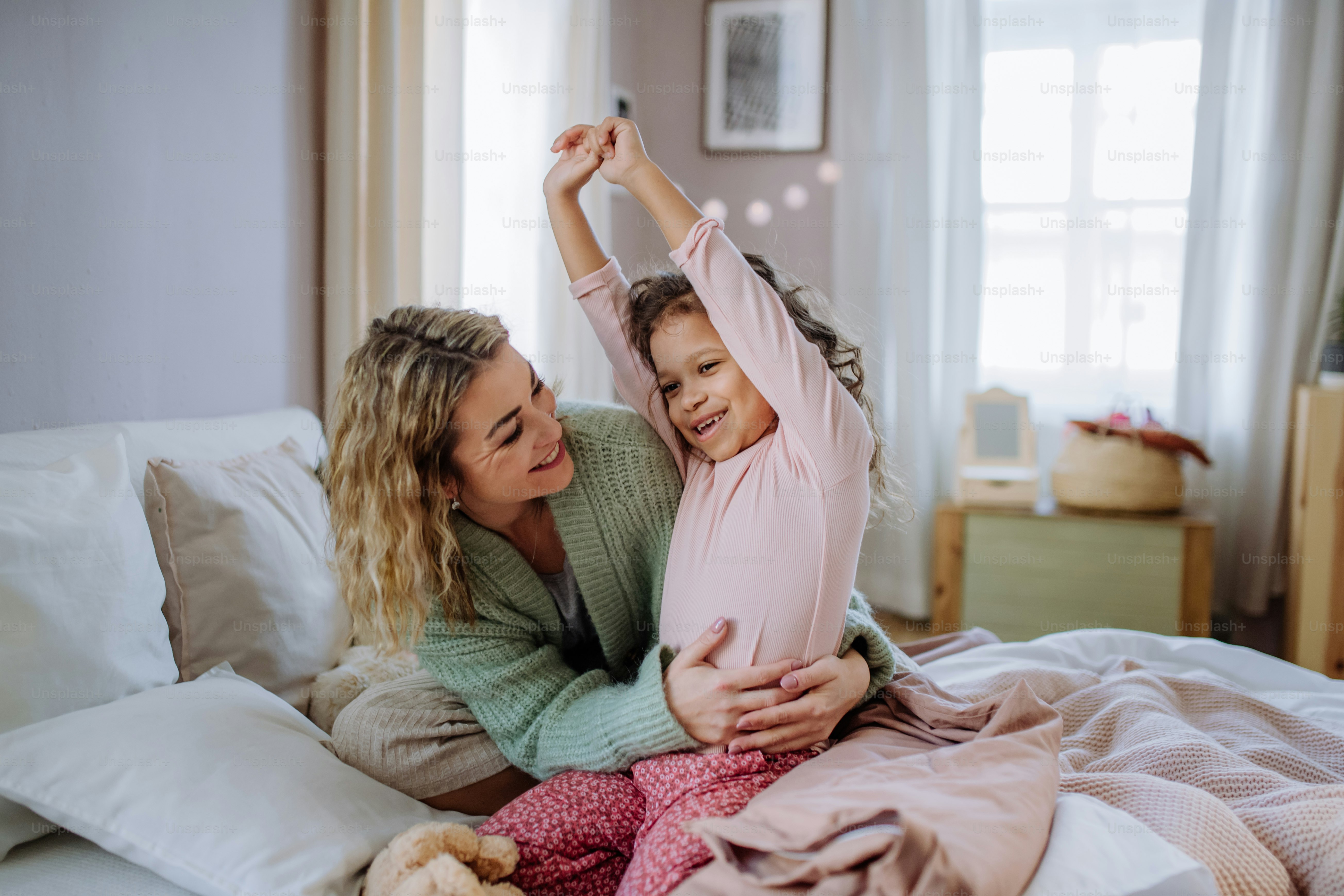 Una madre feliz que acaricia a su pequeña hija estirándose en la cama ...