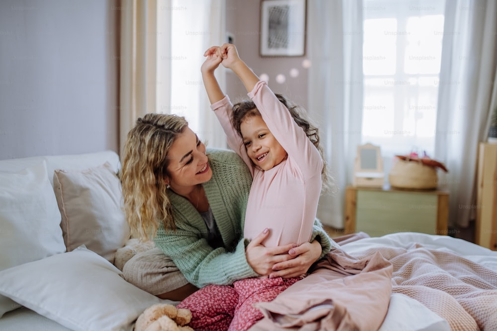 A happy mother hodling her little daughter stretching in bed when waking up in morning.