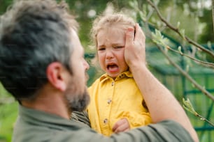 Un padre sosteniendo a su hijita llorando y consolándola en el jardín