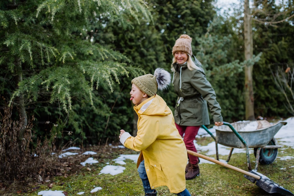 A boy with Down syndrome with his grandmother working in garden in winter together.