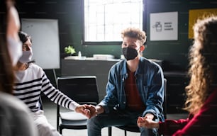 Men and women sitting in a circle during group therapy, holding hands. Coronavirus concept.