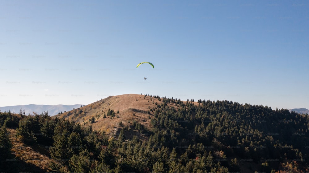 A paraglider flying in the blue sky with mountain in background.