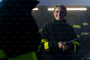 Eine glückliche mittelerwachsene Feuerwehrfrau mit Walkie-Talkie in der Feuerwache in der Nacht.