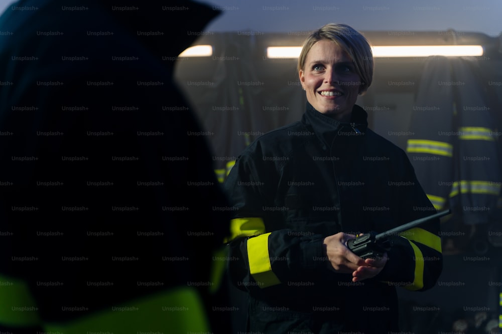 Uma bombeira adulta feliz com walkie talkie no quartel de bombeiros à noite.