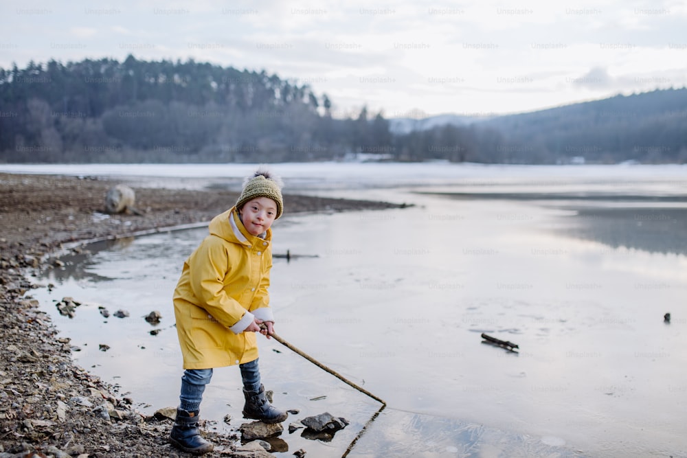 Un niño feliz con síndrome de Down mirando a la cámara afuera junto al lago en invierno.