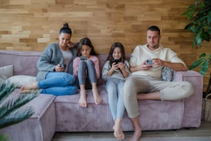Una familia con dos hijas pequeñas, todos usan el teléfono móvil en la sala de estar.
