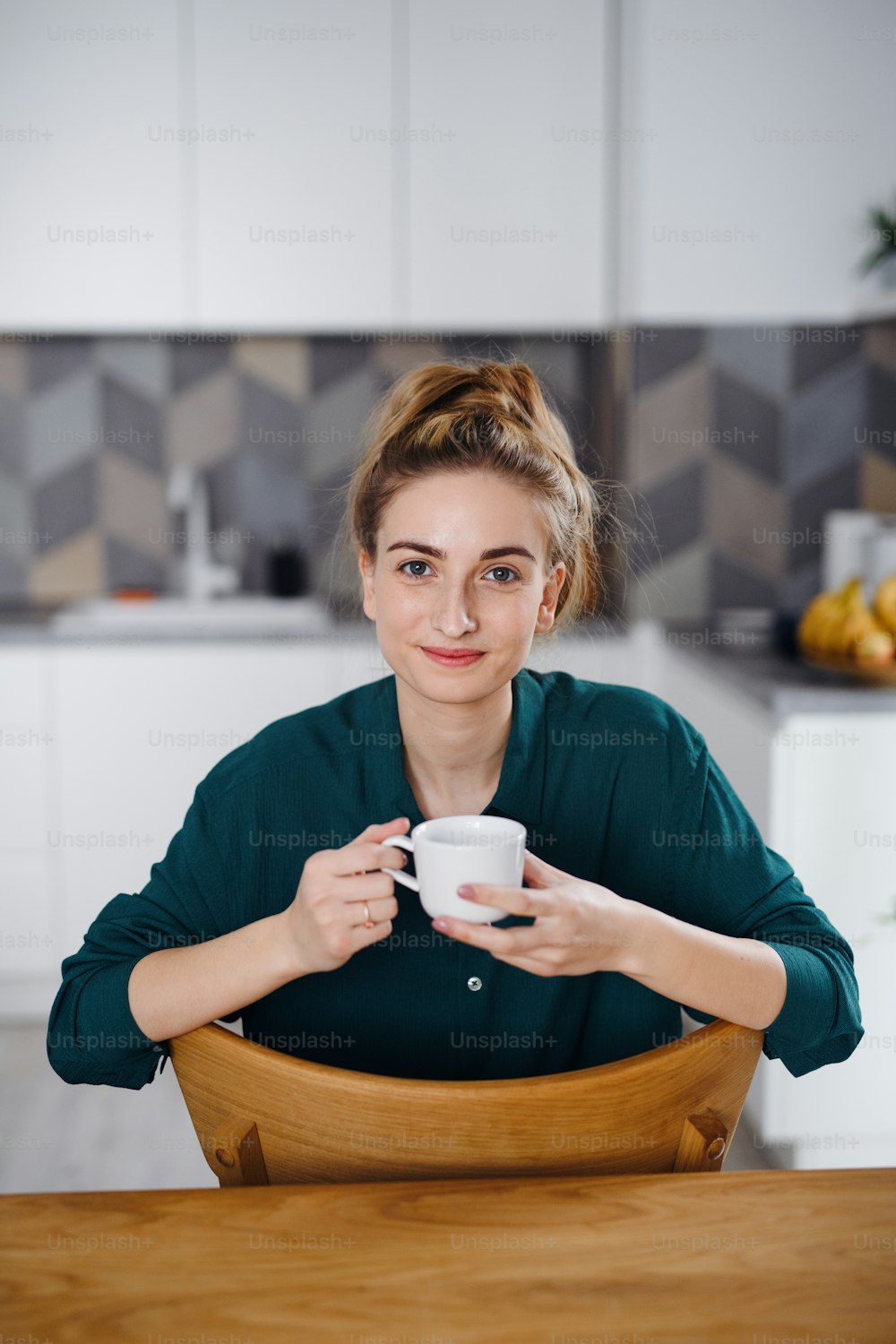 A portrait of happy young woman student drinking coffee at home, looking at camera.
