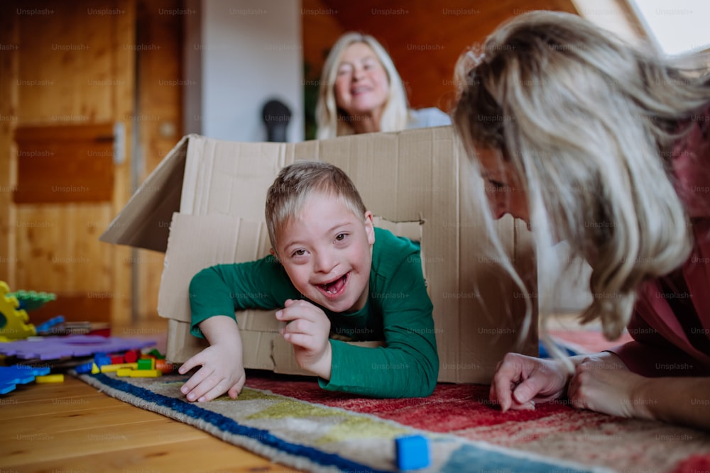 A boy with Down syndrome with his mother and grandmother playing with box together at home.