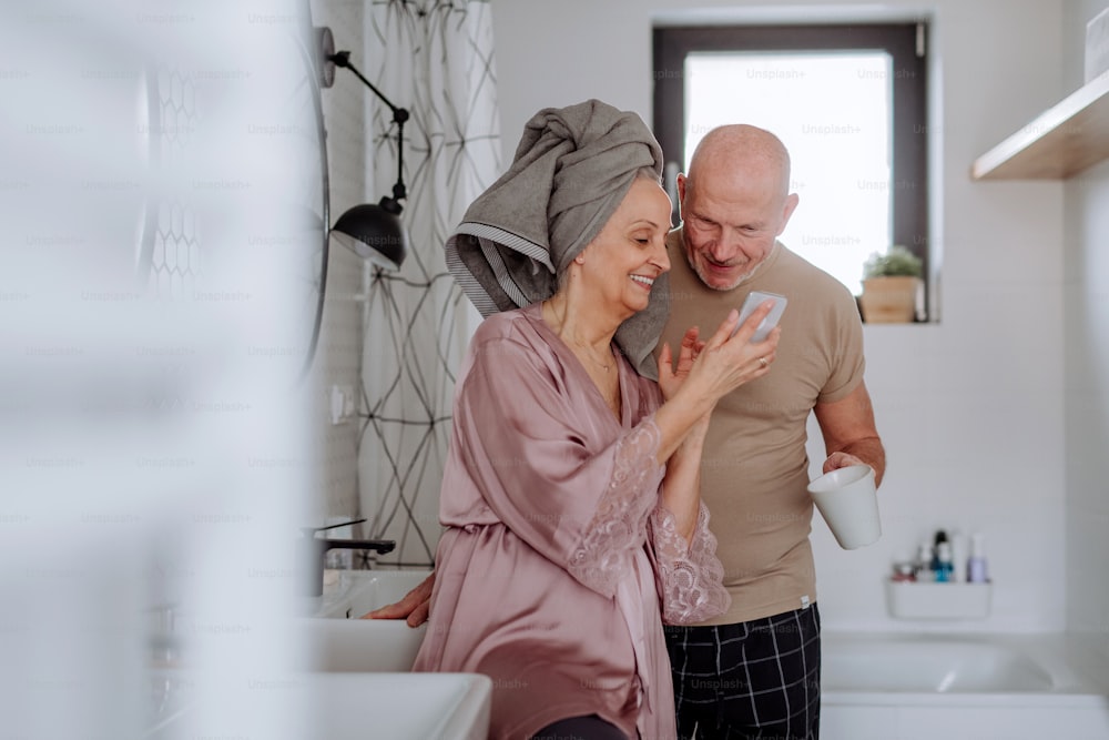 A senior couple in love in bathroom, using smartphone, morning routine concept.