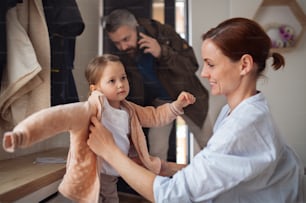 Busy father and mother with small daughter in entrance hall indoors in the morning, leaving for work and nursery school.