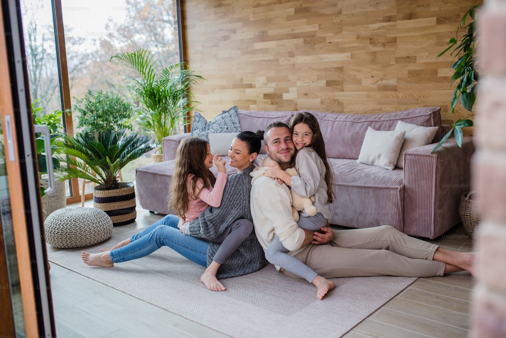 Zwei glückliche Schwestern mit einer Mutter und einem Vater, die zu Hause auf dem Boden sitzen und sich umarmen und in die Kamera schauen