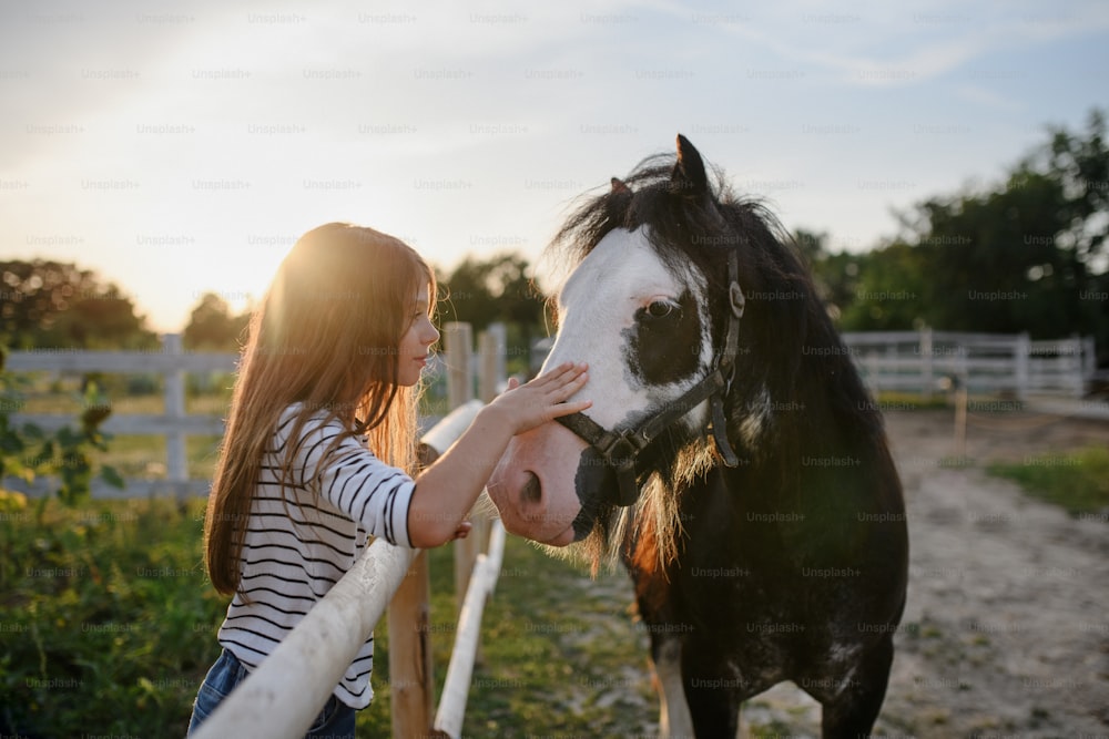 Uma garotinha abraçando cavalo ao ar livre na fazenda comunitária.