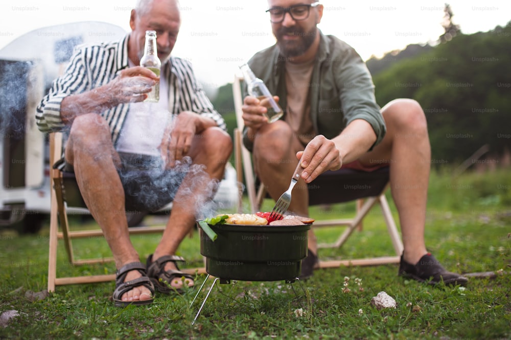 Ein reifer Mann mit älterem Vater spricht auf dem Campingplatz im Freien, Grillen auf Wohnwagenurlaub.