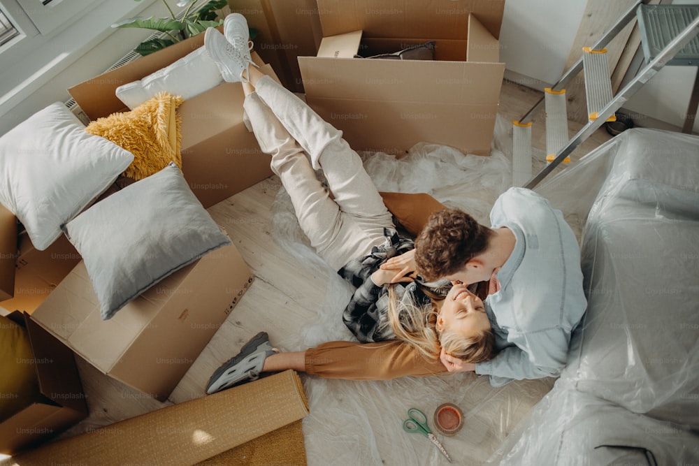 Una vista superior de una alegre pareja joven en su nuevo apartamento, sentados en el suelo y abrazándose. Concepción de la mudanza.