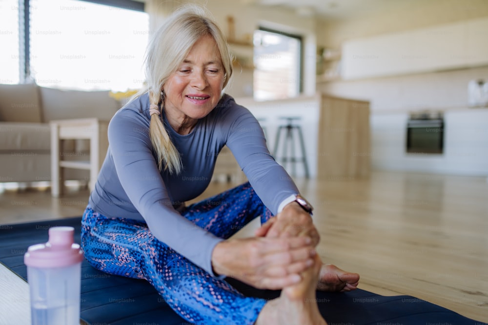 A fit senior woman doing stretching exercise at home, active lifestyle concept.