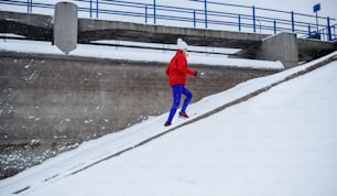 A side view of active senior woman running up the stairs outdoors in snowy winter.