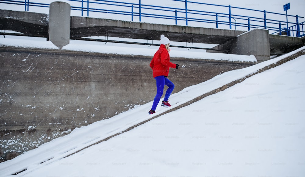 Una vista lateral de una mujer mayor activa corriendo por las escaleras al aire libre en invierno nevado.