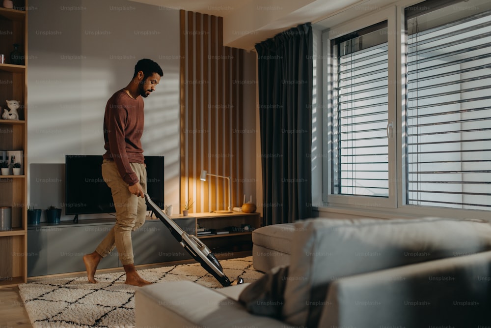 Ein junger Mann saugt Teppich im Wohnzimmer