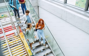 A top view of university students walking down the stairs indoors, talking.