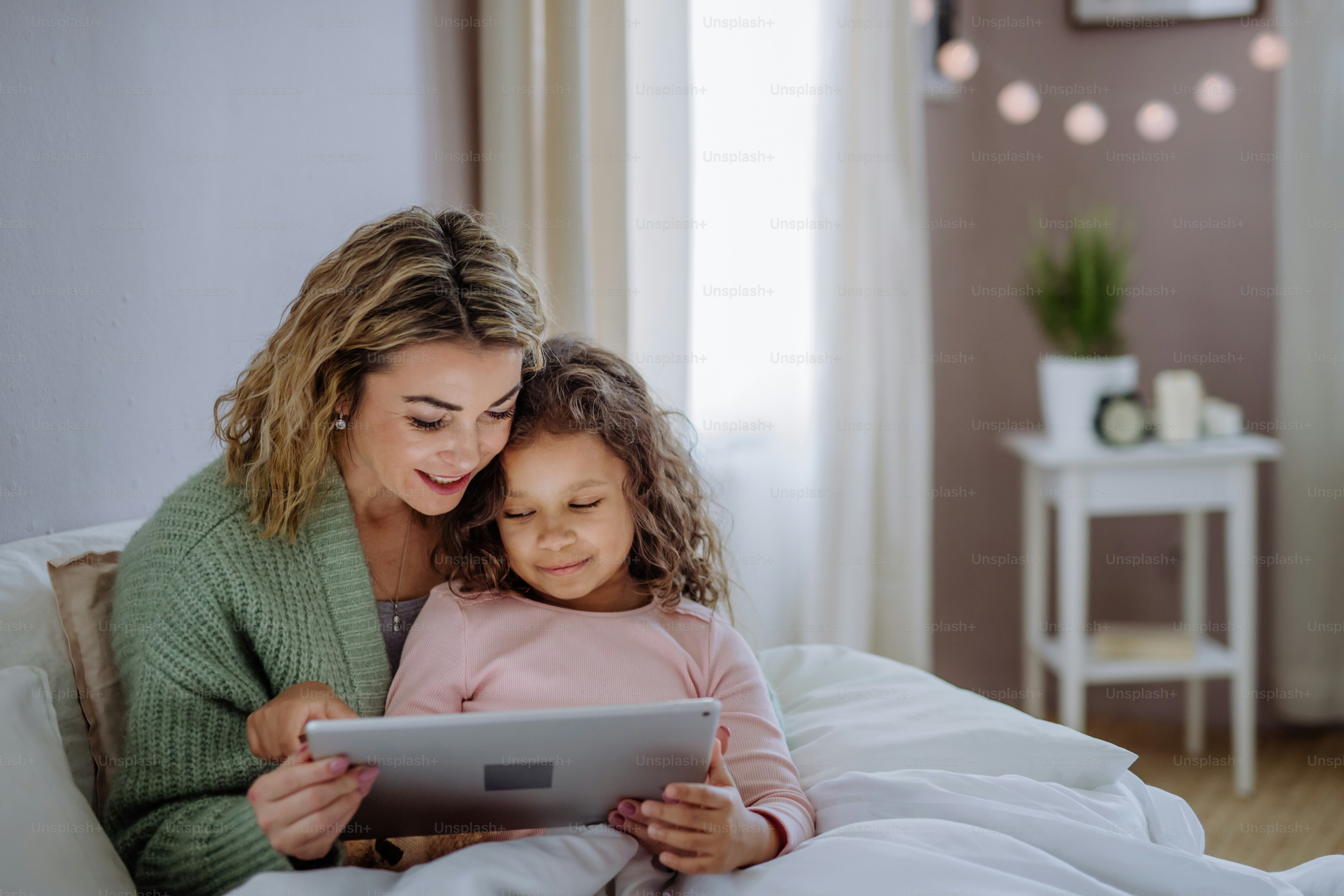 Foto Una madre feliz con su hija pequeña acostada en la cama y usando ...