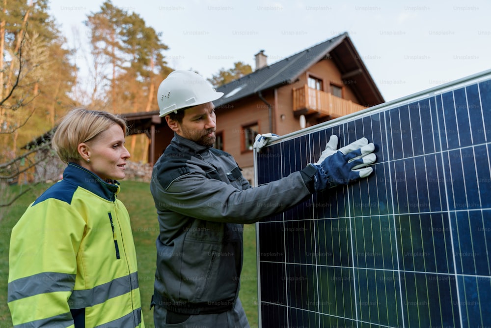 Ein Handwerker Solarinstallateur diskutiert mit seinem Kollegen am Solarmodul vor dem Einfamilienhaus.