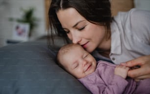 Una madre joven y feliz besando a su bebé recién nacida, acostada en el sofá en el interior de su casa.