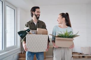 A young couple with boxes looking at each other when moving in new flat, new home and relocation concept.