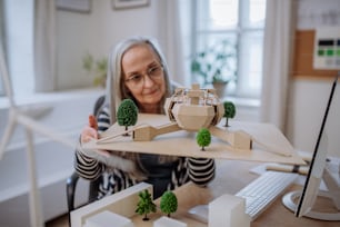 A senior woman architect holding model of modern eco buliding in office