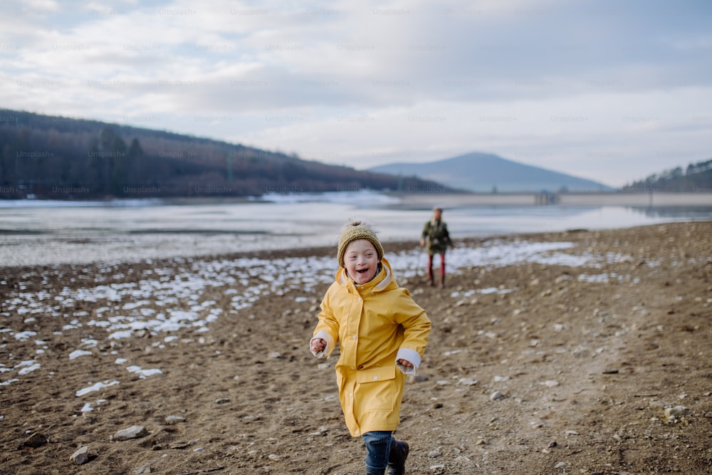 A happy little boy with Down running outside by lake in winter.
