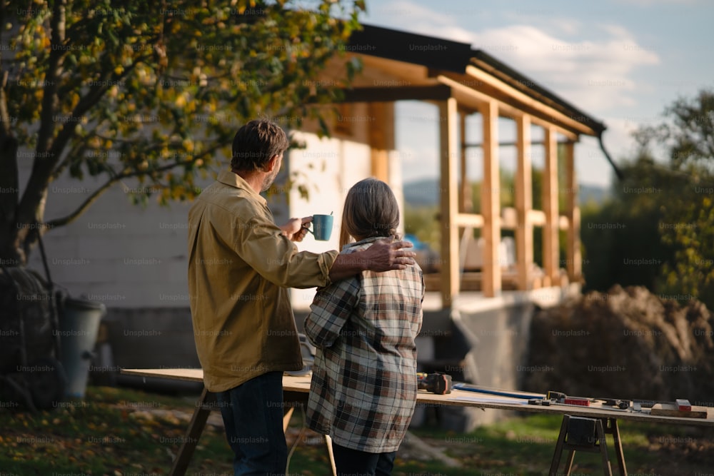 A mature couple looking at their new house under construction, planning future and dreaming.