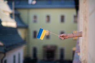 A mão de uma menina enfiando a bandeira ucraniana para fora da janela solidariedade com a Ucrânia no conceito de guerra.