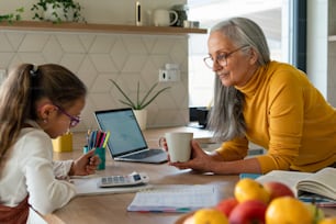 A small girl with senior grandmother doing homework at home.