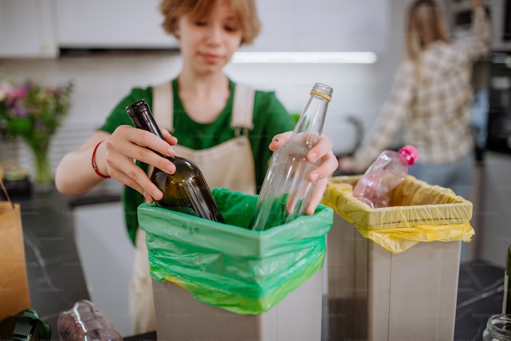 Una adolescente tirando botellas de vidrio en un contenedor de reciclaje en la cocina.