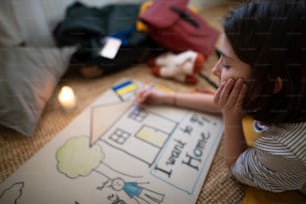 A sad Ukrainian refugee child missing her home and drawing her family. Ukrainian war concept.