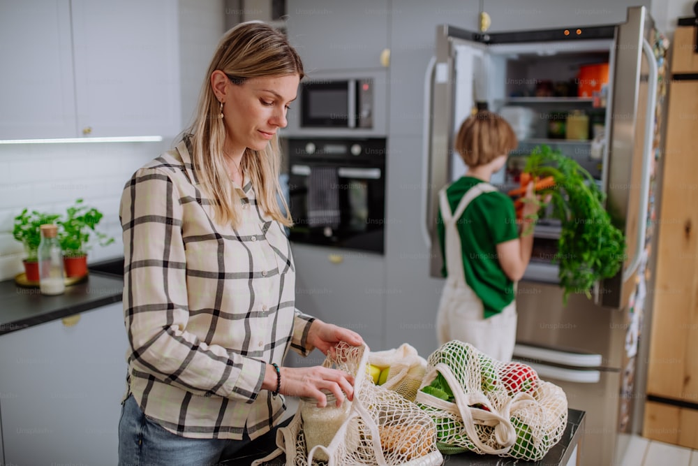 Una madre che disimballa il cibo locale in un imballaggio a rifiuti zero dal sacchetto con l'aiuto della figlia in cucina a casa.