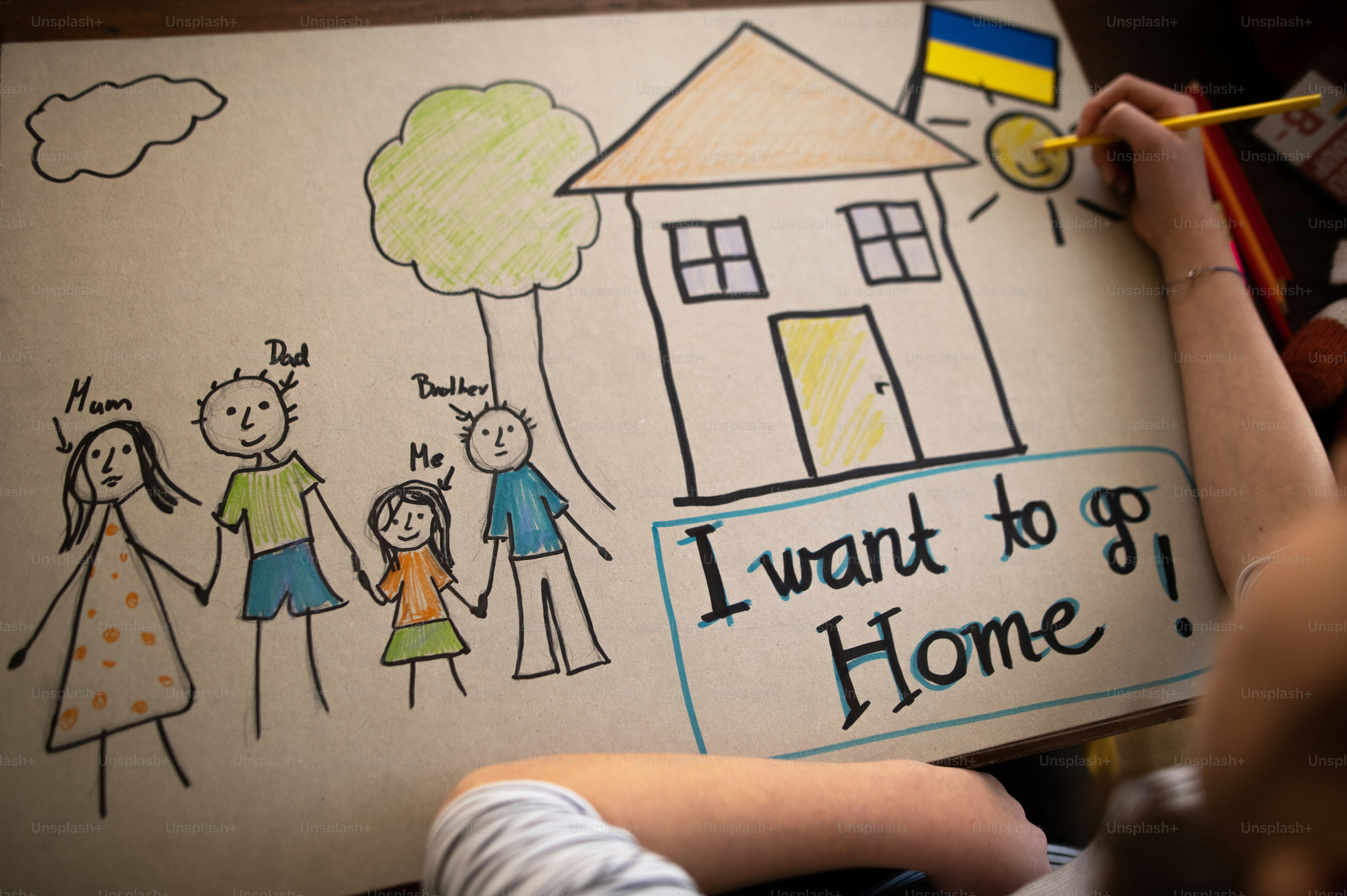 A top view of Ukrainian refugee schoolgirl missing home and drawing her family. Ukrainian war concept.