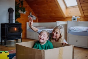 A boy with Down syndrome with his mother and grandmother playing with box together at home.