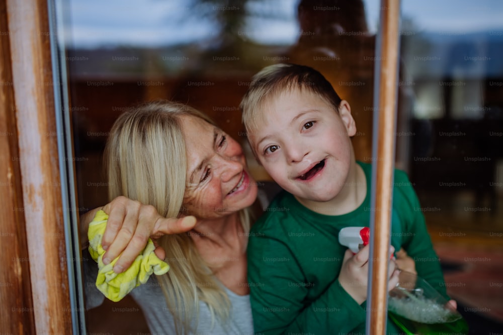 Ein Junge mit Down-Syndrom mit seiner Mutter und Großmutter putzt Fenster zu Hause.