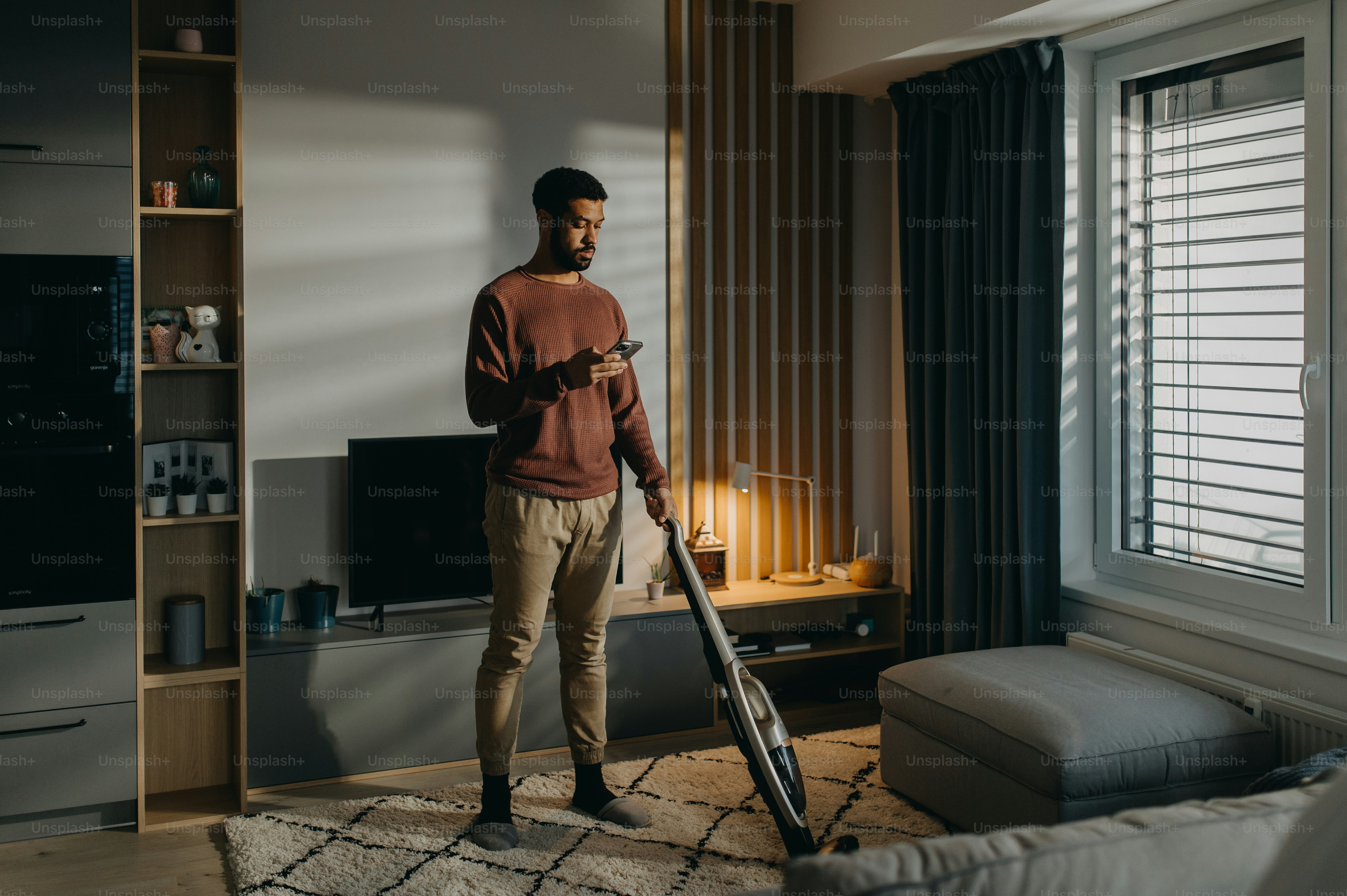 Un jeune homme passe l’aspirateur avec un aspirateur dans le salon