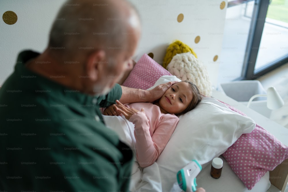 A grandfather taking care of his ill granddaughter lying in bed.