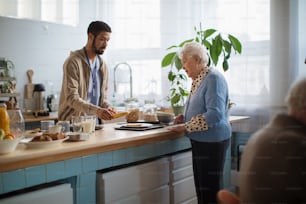 Un joven cuidador sirve el desayuno a una anciana en un centro de atención en un hogar de ancianos.