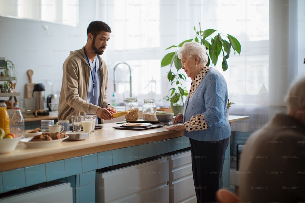 A young caregiver serving breakfast to elderly woman in nursing home care center.