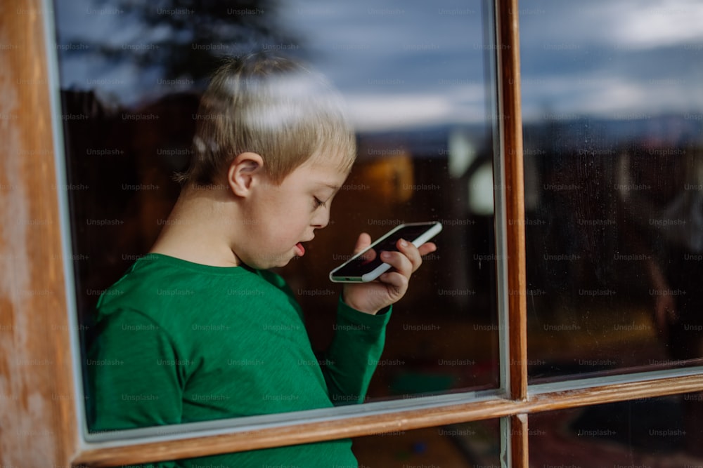 A sad little boy with Down syndrome using smartphone at home