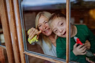 A boy with Down syndrome with his mother and grandmother cleaning window at home.