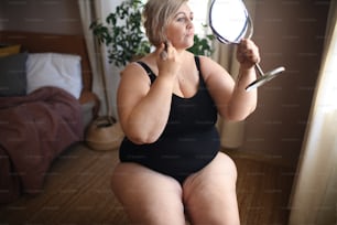 太った女性が座って家で鏡を見ている、セルフケアのコンセプト。