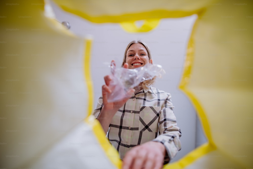 Imagen desde el interior de una bolsa amarilla de reciclaje de una mujer tirando una botella de plástico para reciclar.