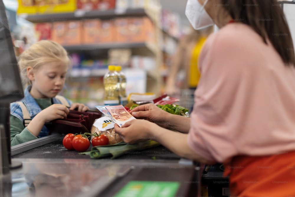 Close-up de uma menina loira pagando por compras de supermercado no supermercado.