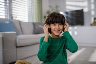 Ein glücklicher multirassischer Junge mit Kopfhörern, der zu Hause Musik hört.
