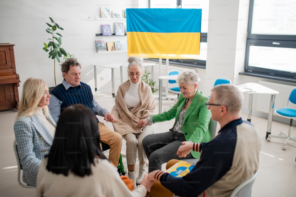 Un gruppo di anziani che si tengono per mano e pregano insieme per l'Ucraina nel centro comunitario della chiesa.